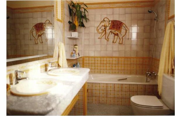 Baño con zócalo en tonos amarillos, y motivo de elefante en bañera